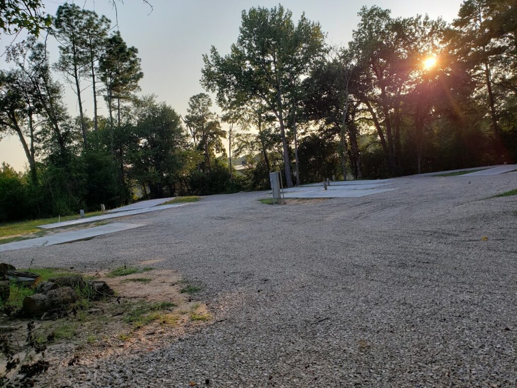 Wide shot of RV spots 5 through 12 at sunset with full hookups and concrete pads beneath a tree-lined horizon